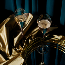 Load image into Gallery viewer, Two signature champagne flutes pictured on a gold textured cloth and a tray, with a blue curtain in the background.