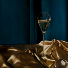 Load image into Gallery viewer, A signature champagne flute pictured on a gold textured cloth and a tray, with a blue curtain in the background.